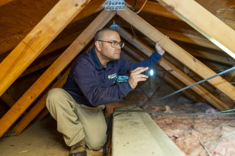 Pest control technician inspecting attic with flashlight for signs of termite infestation