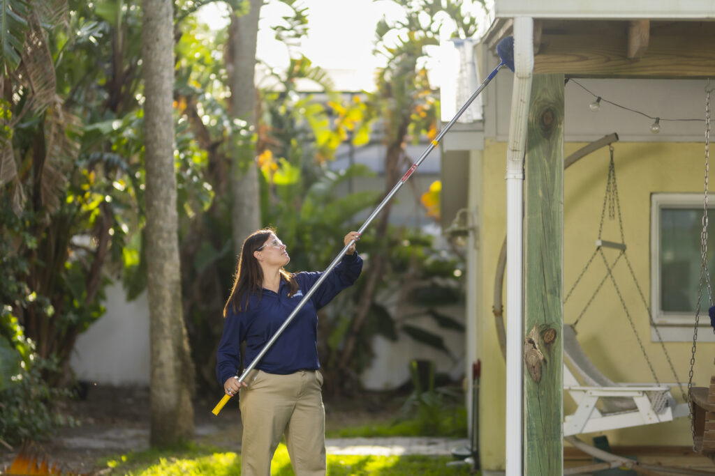 Pest control technician treating roofline and eaves of a Florida home to prevent spiders, wasps, and other outdoor pests