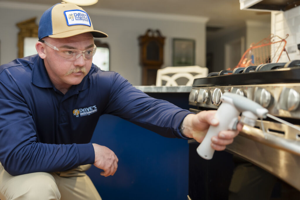 Pest control technician inspecting kitchen stove area in a Florida home to prevent cockroaches and household pests
